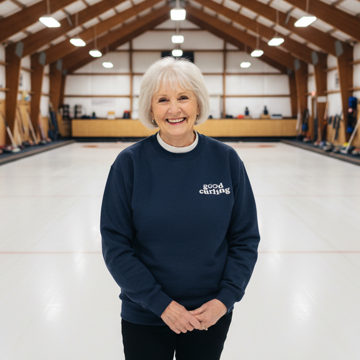 Woman wearing a navy blue sweatshirt with 'good curling' text in a curling rink.