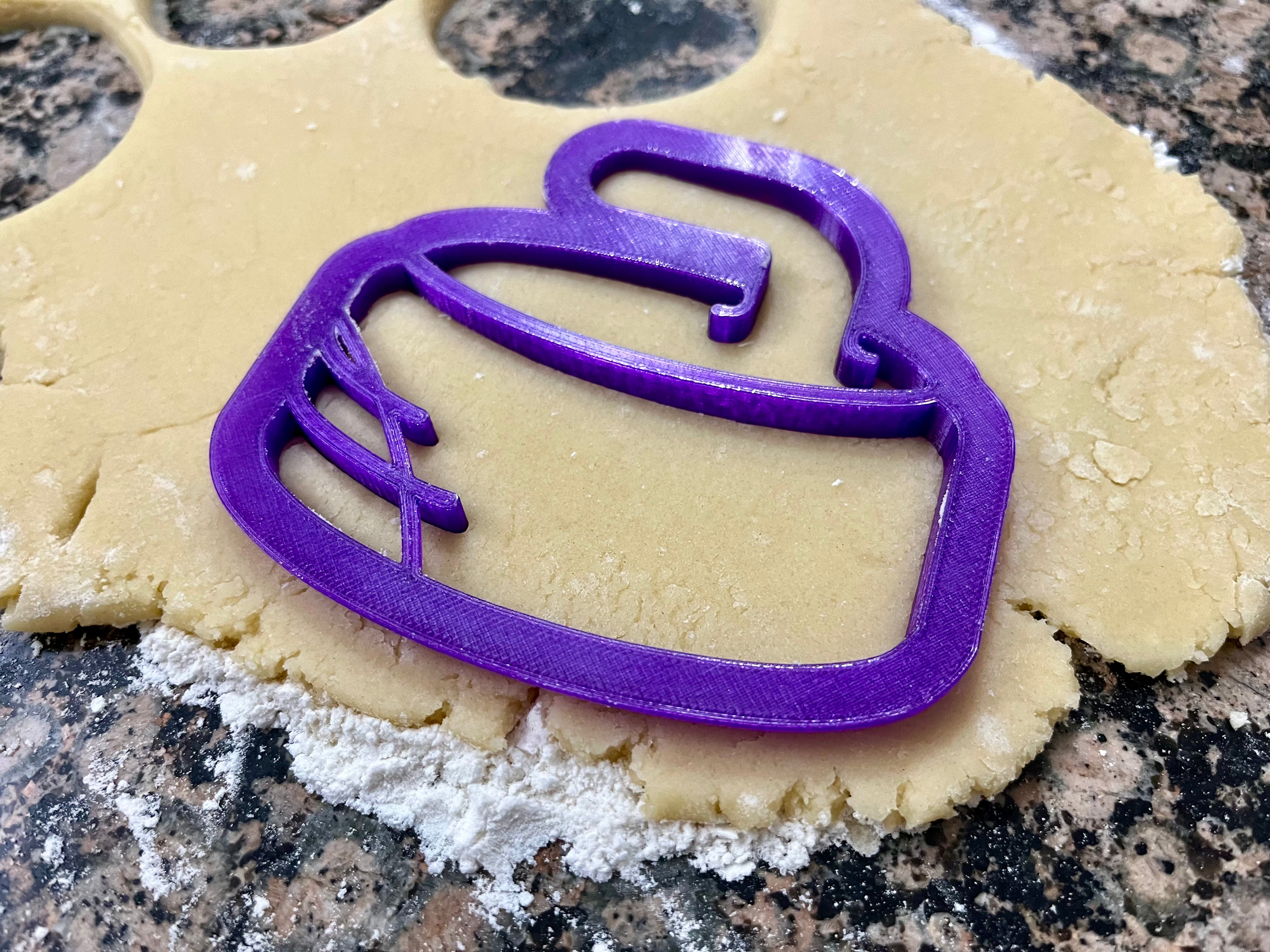 purple cookie cutter shaped like a curling rock placed in cookie dough